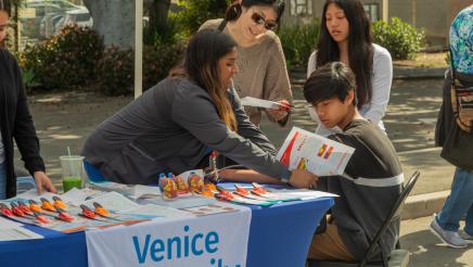 Venice Family Clinic booth staffer providing health service to attendee